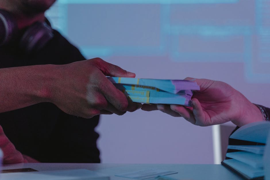 Close-up of hands exchanging money, highlighting financial exchange in a dimly lit setting.